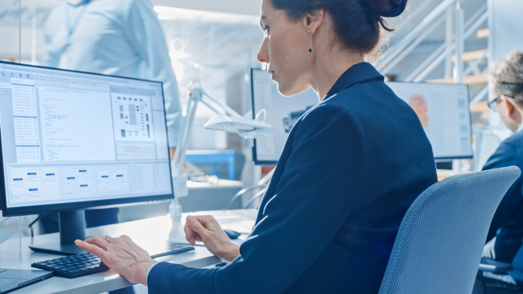 A woman working at a computer in a modern office, analyzing data and software on her screen.