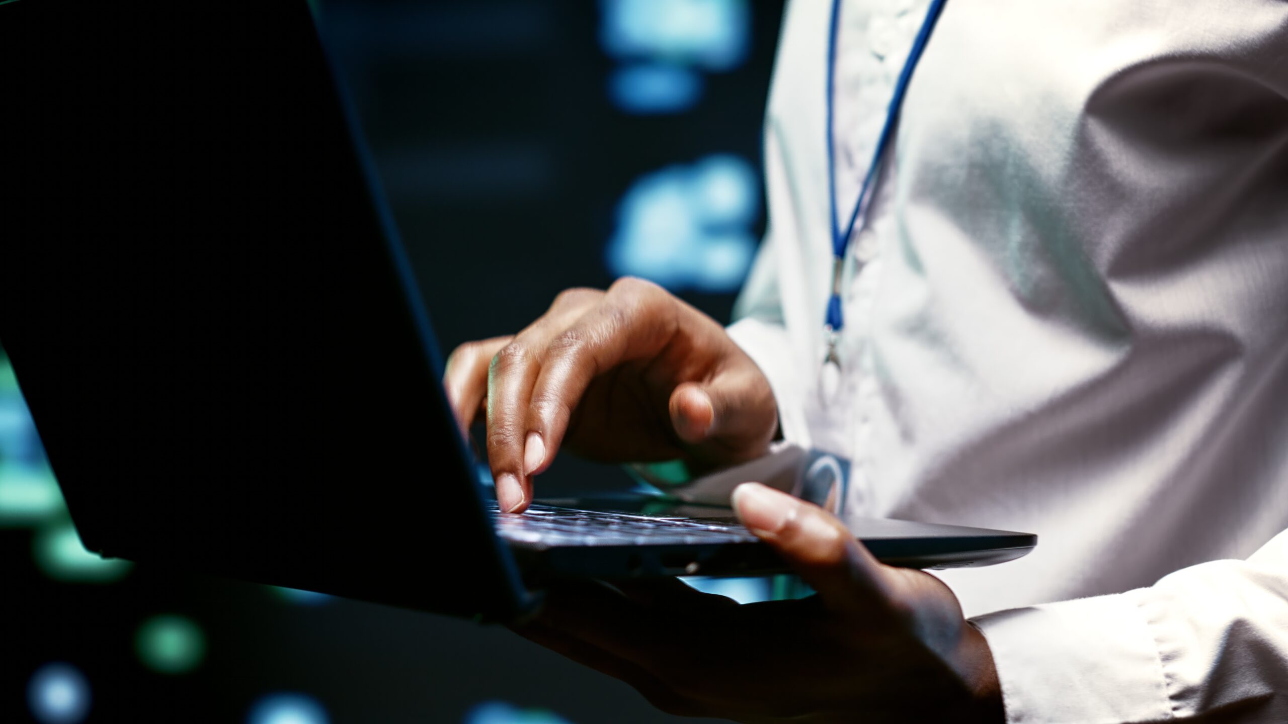 Close-up of a person typing on a laptop, with a blurred background of data or code.