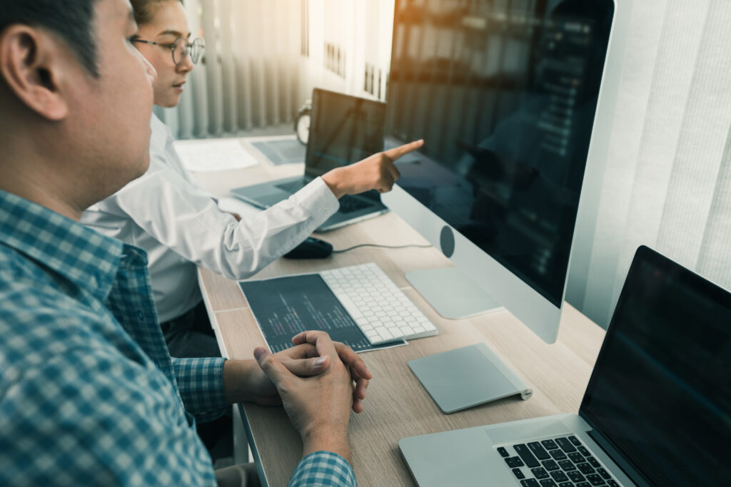 Two programmers collaborating on data quality in AI/machine learning while working on code displayed on a large computer monitor.