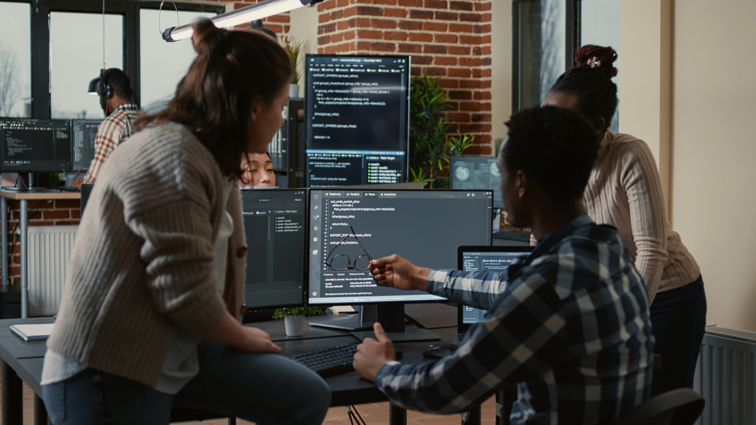 A group of programmers collaborating in an office, reviewing machine learning code on multiple screens.